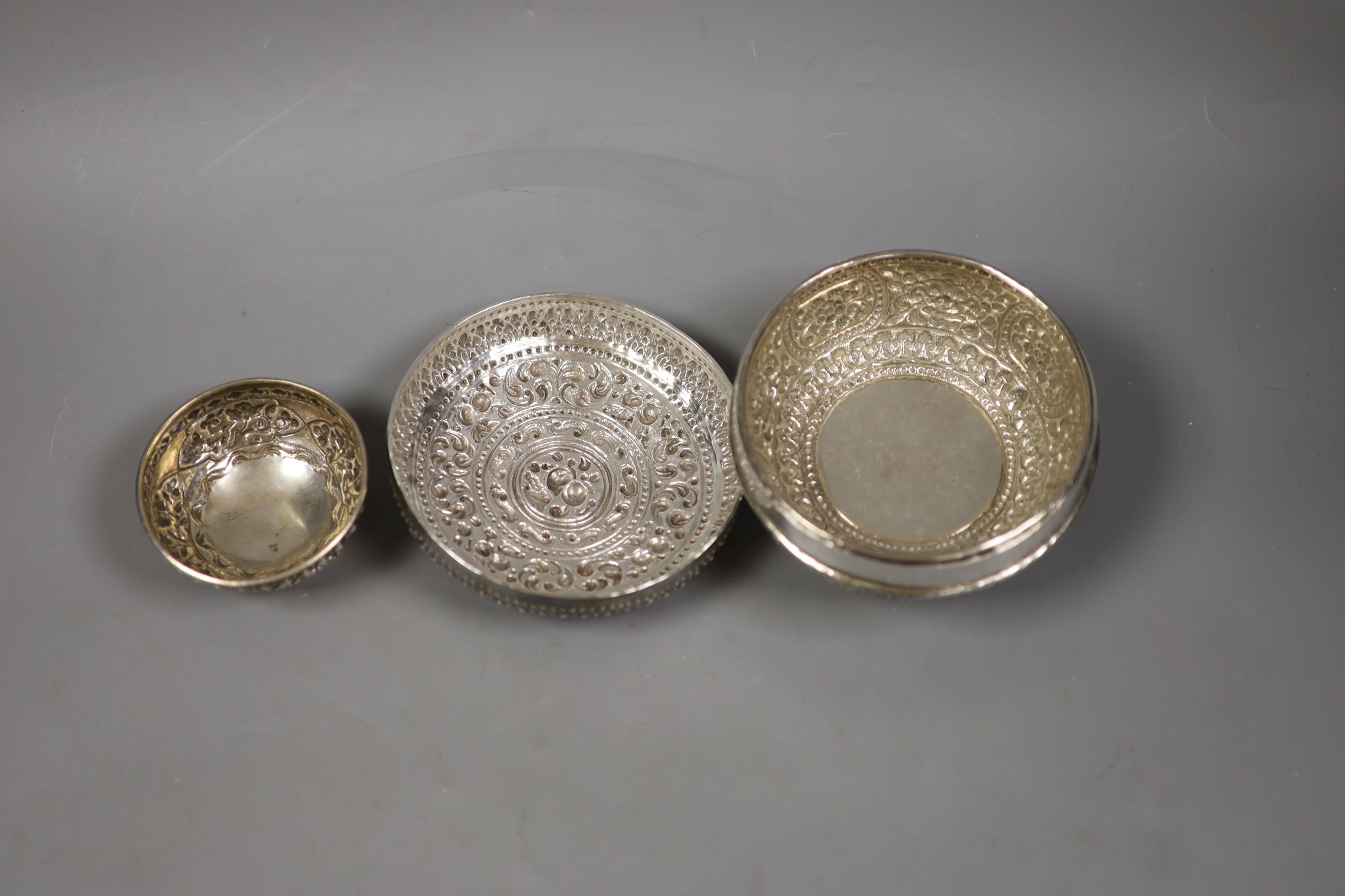 An Indonesian embossed white metal bowl and cover and two similar smaller bowls, largest diameter 13.5cm